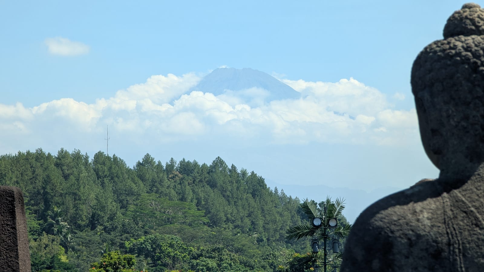 Mount Merapi volcano peeking through clouds beside Borobudur