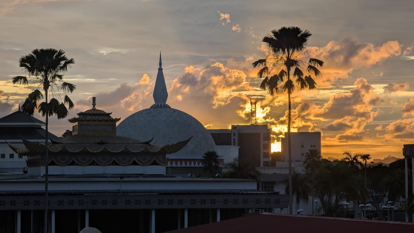 Mosque domes silhouetted against a golden sunset sky with palm trees