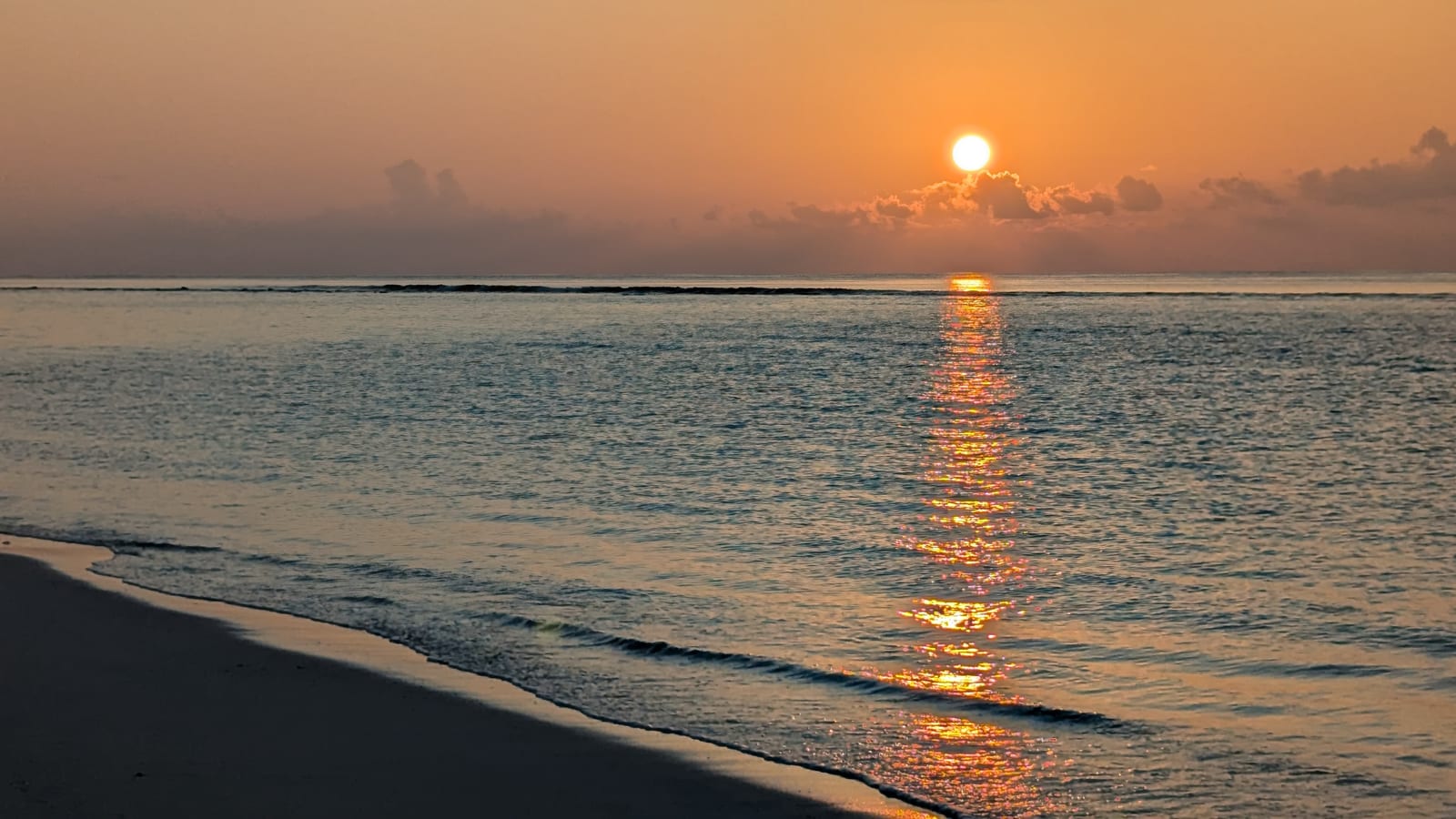 Sunrise over a sandbar with orange sky reflected on calm water
