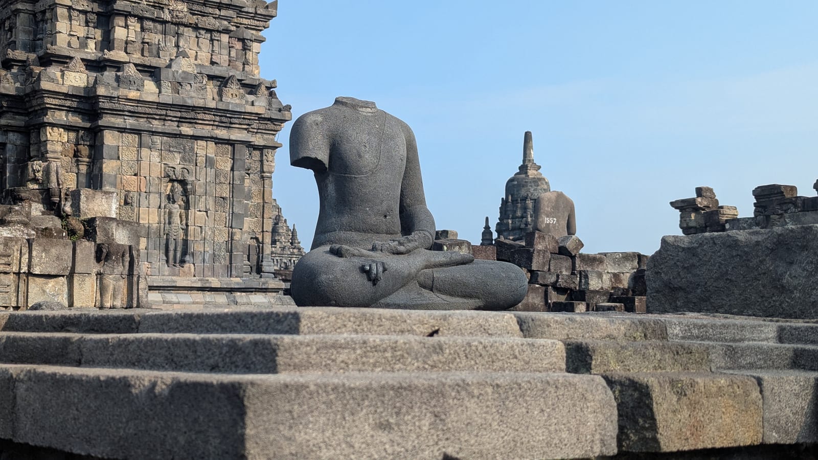 A headless meditating statue with Prambanan temple in the background