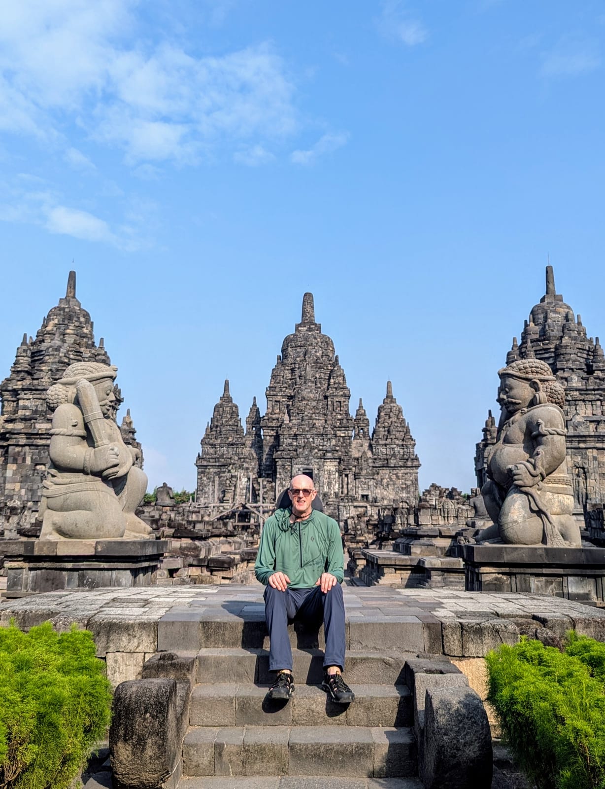 A traveler sitting on Prambanan temple steps flanked by guardian statues