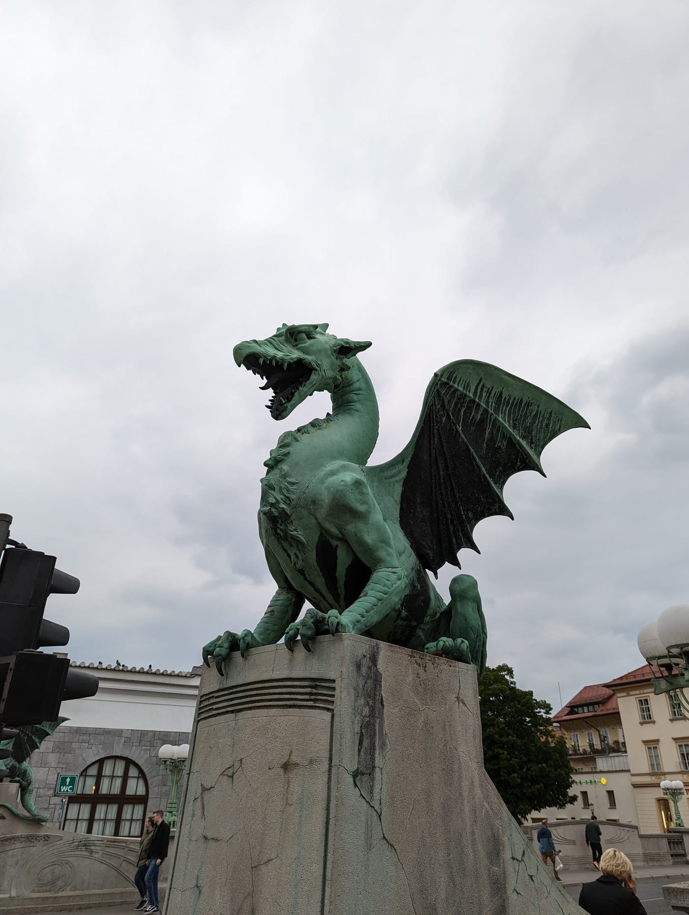 The green dragon statue on Ljubljana Dragon Bridge against a cloudy sky
